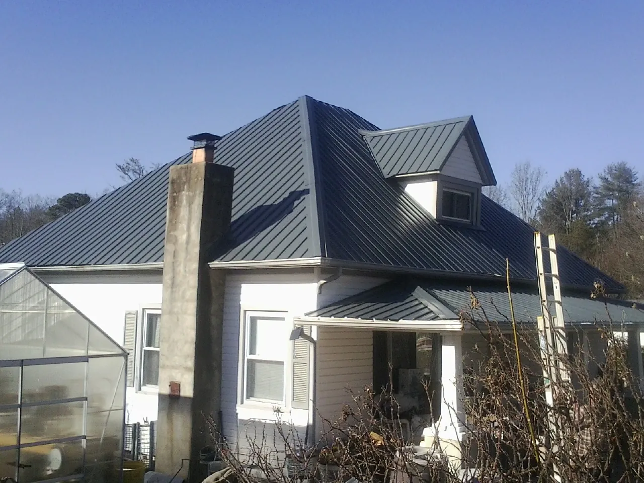 Dark blue standing seam metal roof on a white farmhouse with dormer — Slate & Tile Roof Repair by Roofing Brothers in Springs