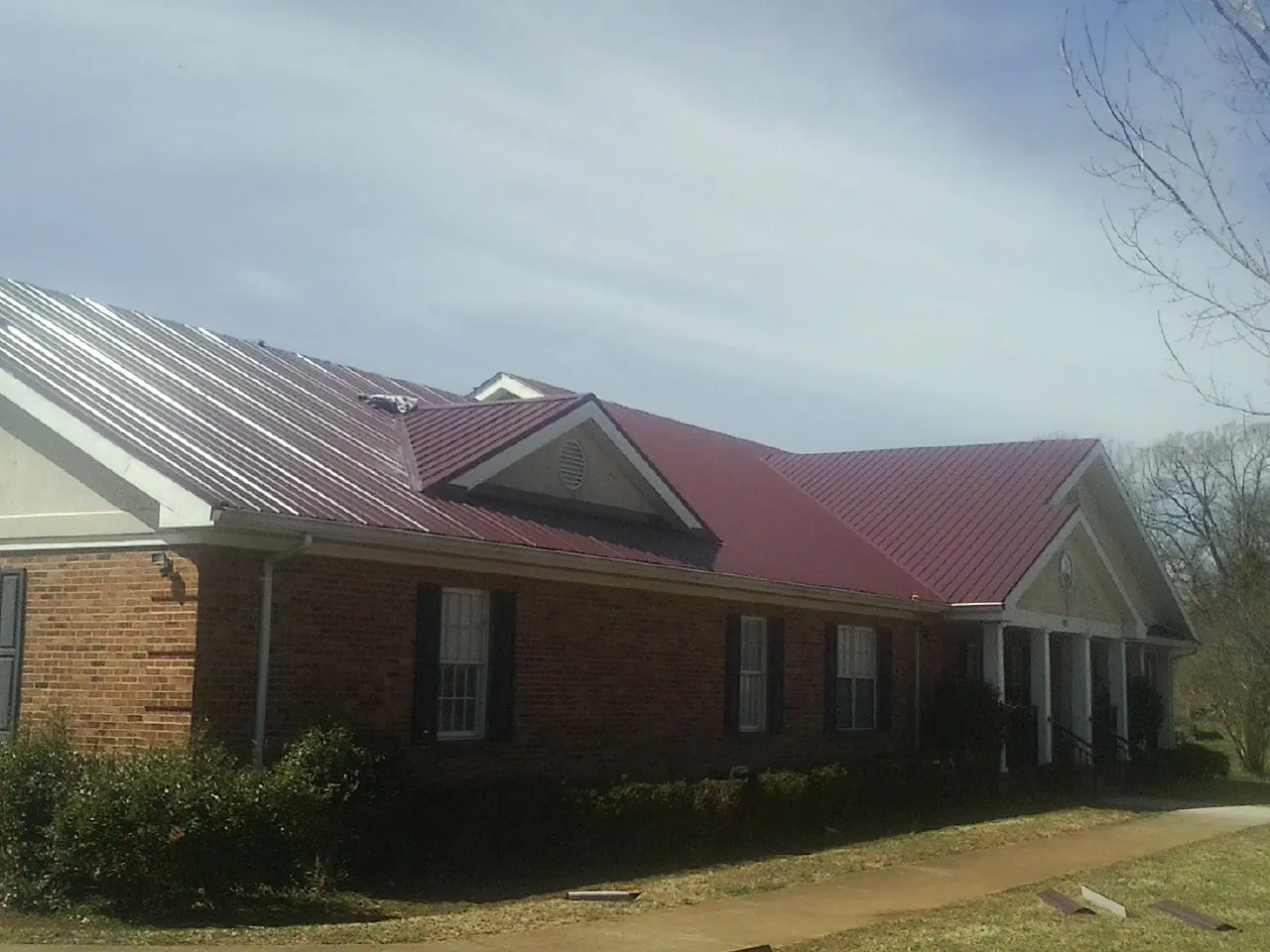 Red metal roof with gabled entries on a long brick building, from a Hail Damage Roof Repair job in Springs