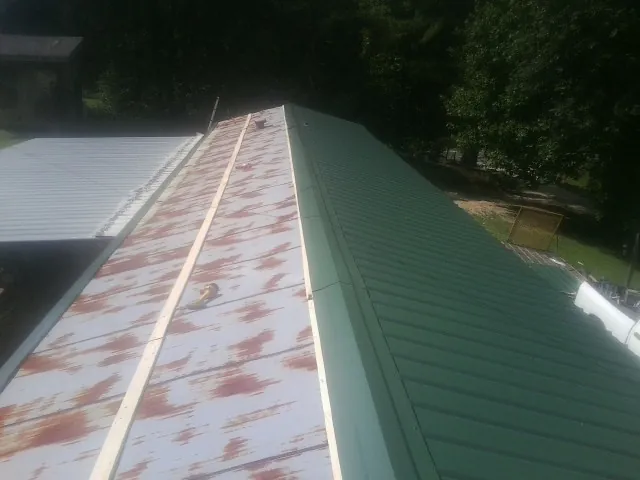 Old rusted panels beside newly installed green metal roofing — Wind Damage Roof Repair by Roofing Brothers in Springs