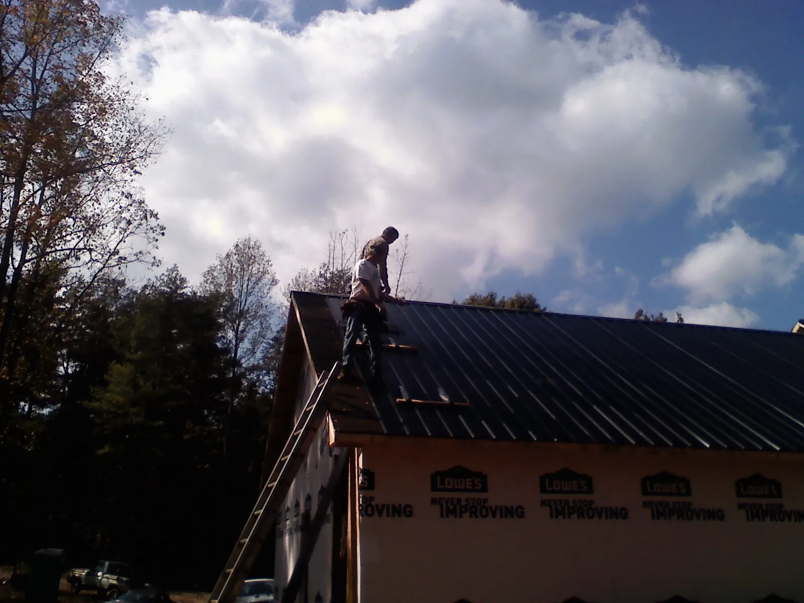 Roofer fastening dark metal panels high against a cloudy sky, from a Roof Inspection job in Springs