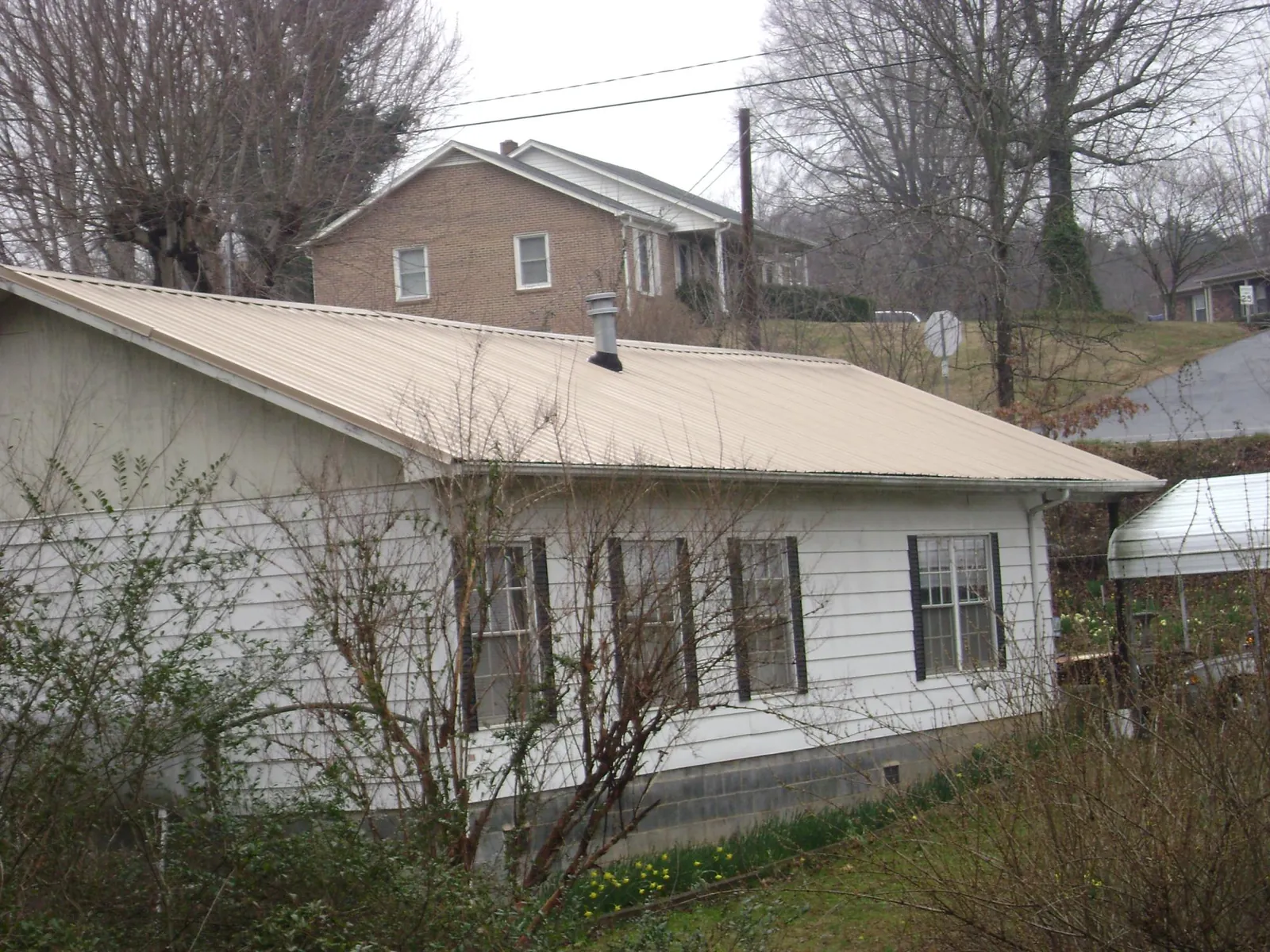 Tan metal roof on a white sided house set into a hillside — Commercial Roofing by Roofing Brothers in Springs